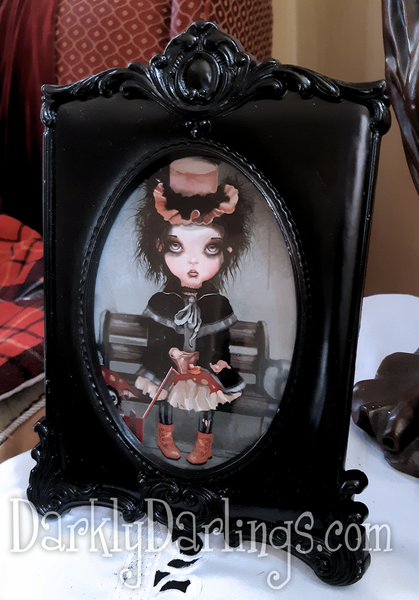 A victorian goth girl and her dolls on a bench in a black frame